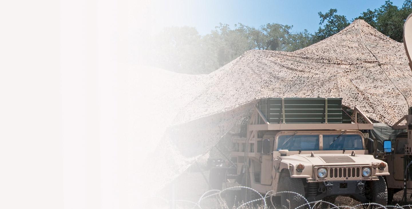 HUMVEE under a camo tent surrounded by barbed-fencing 